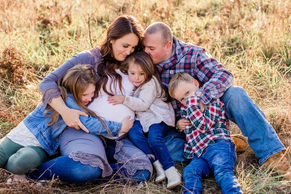 Family snuggled together on the ground in a field