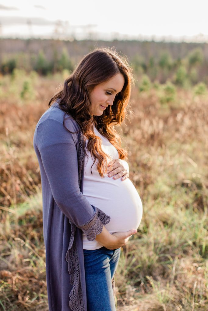 Pregnant woman standing in a field holding on to her belly at sunset