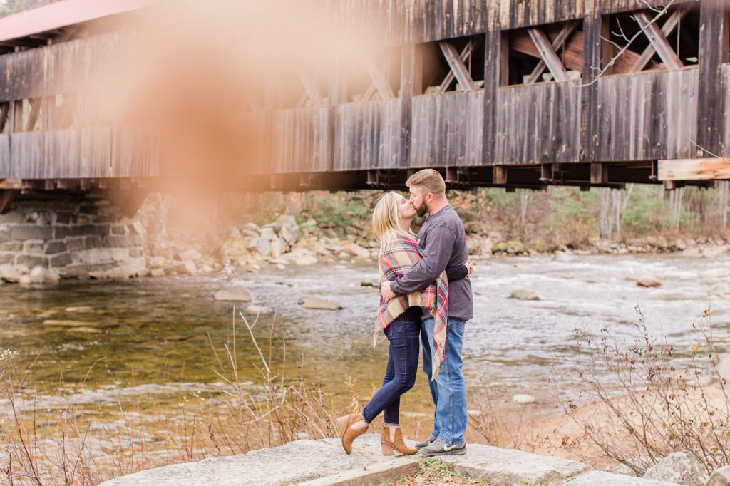 Man and woman kissing in front of covered bridge