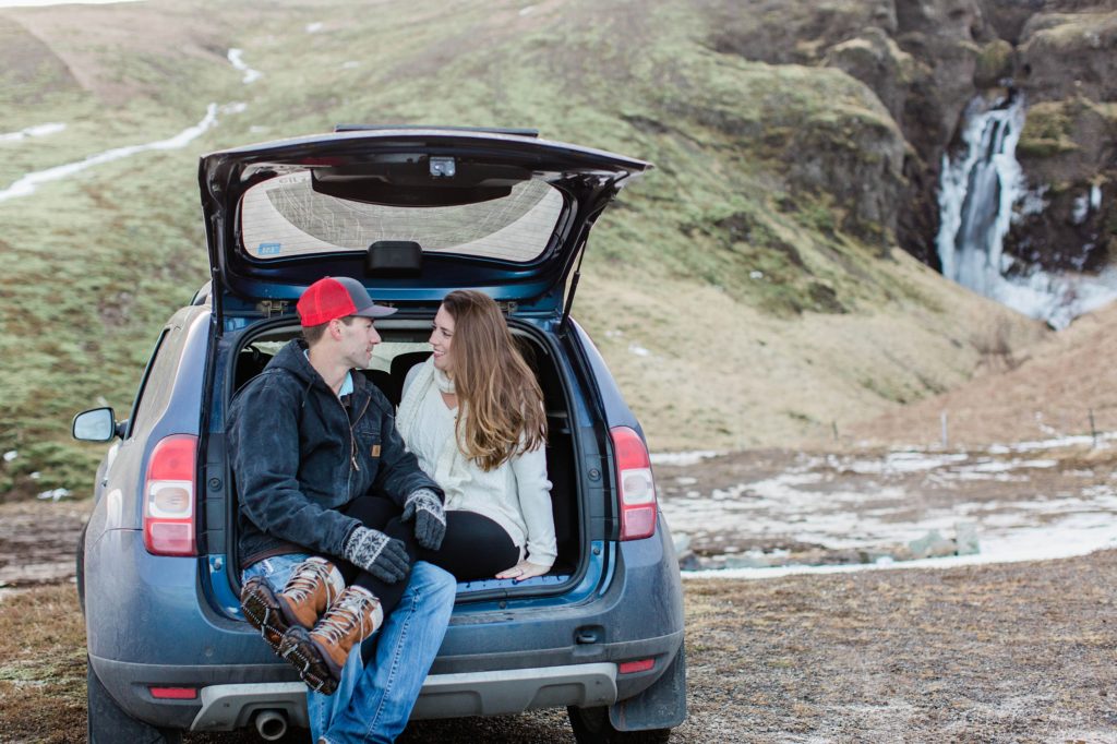 Man and woman sitting together in the back of a jeep in front of a waterfall in Iceland