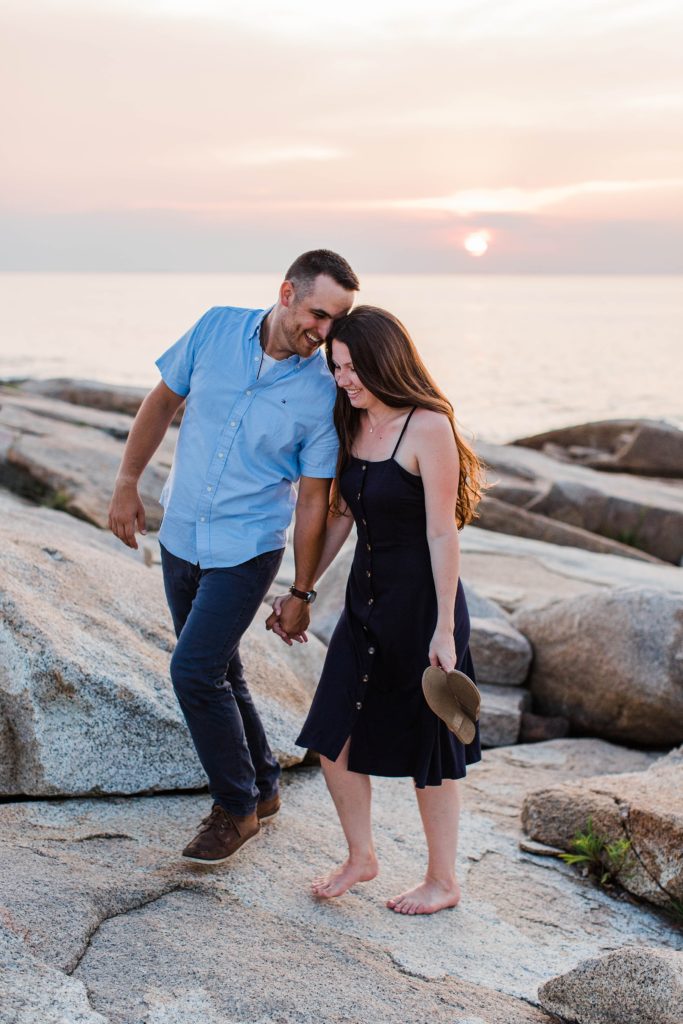 Man and woman standing on rocks at sunset by the ocean