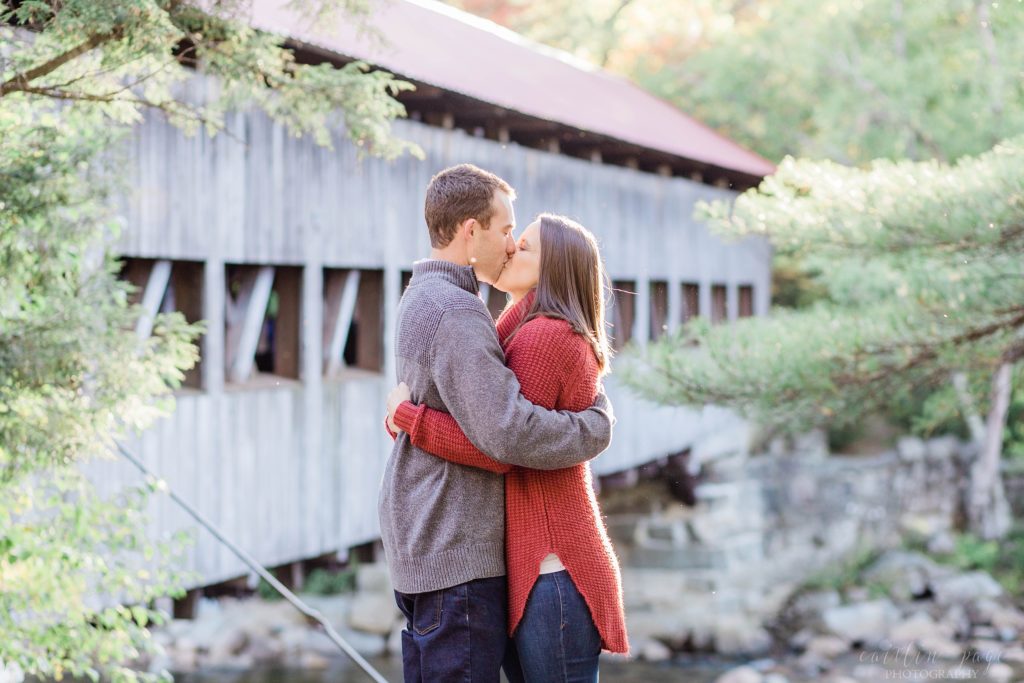 Man and woman kissing in front of covered bridge