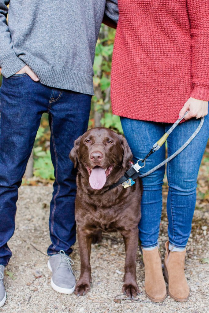Man and woman standing together with their chocolate lab sitting between them