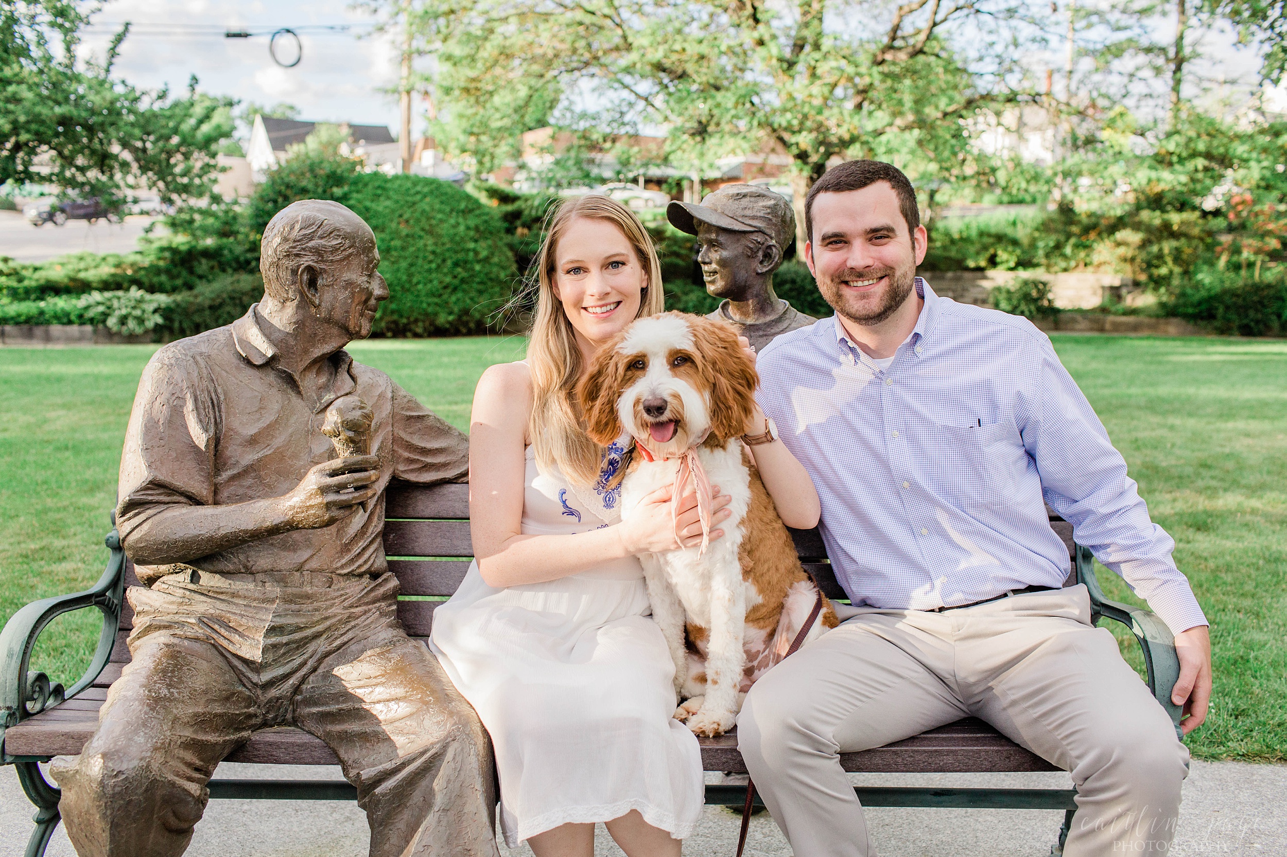 Man, woman and dog sitting on bench with bronze statues