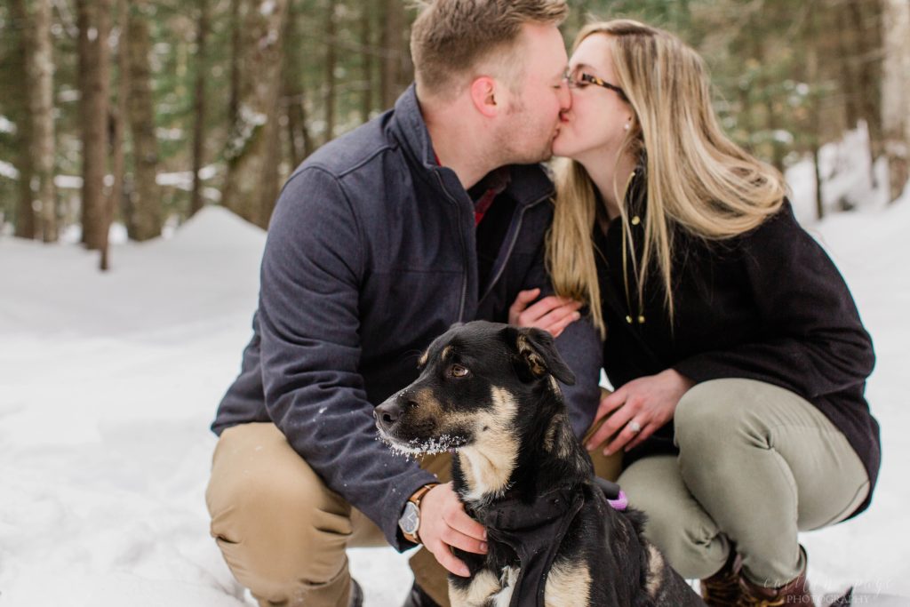 Man and woman kissing in the snow with their puppy