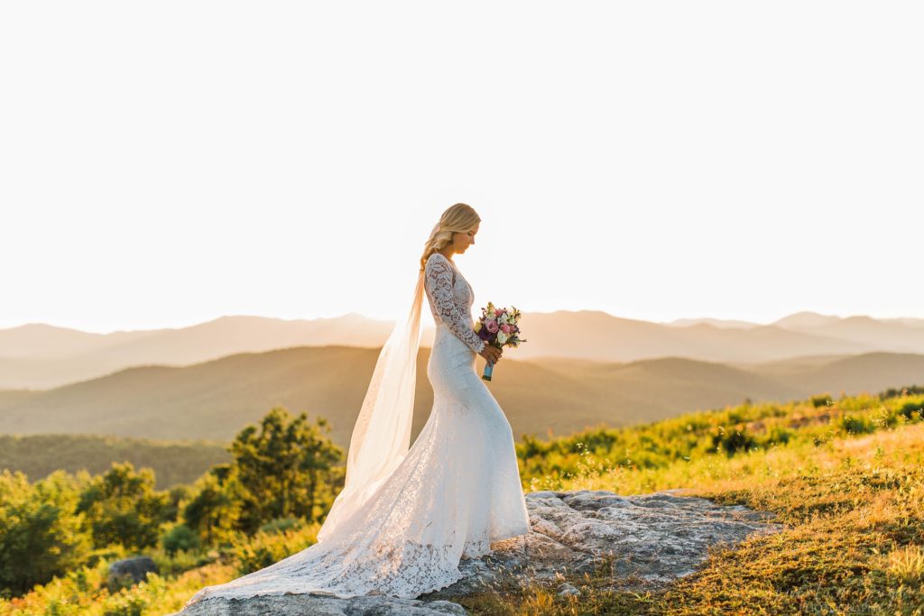 Woman standing on a mountaintop in a lace wedding gown