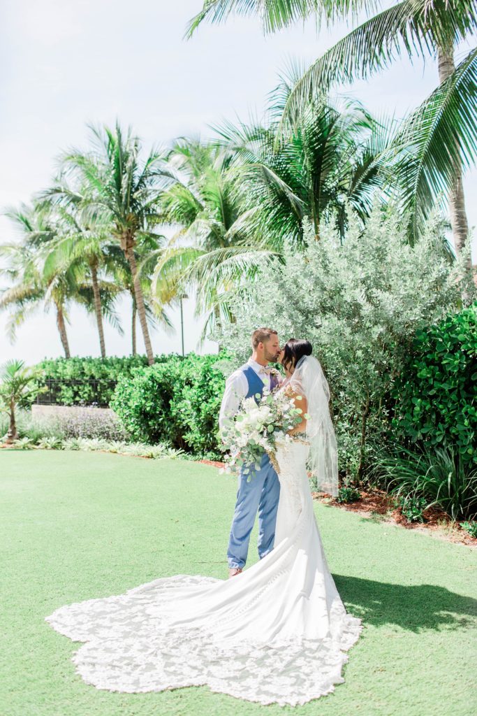 Bride and groom kissing on lawn with palm trees