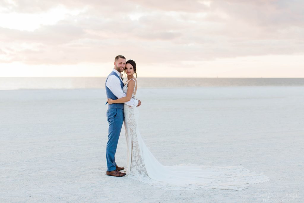 Bride and groom standing on beach at sunset