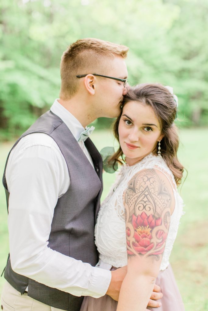 Groom kissing bride on the forehead with quarter sleeve tattoos