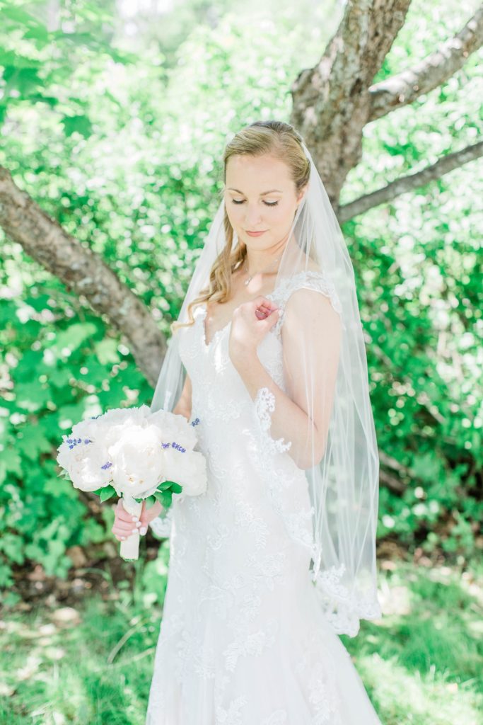 Bride holding white peony bouquet with lace trimmed wedding veil