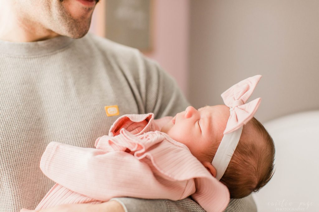 Baby girl being held by dad in pink outfit