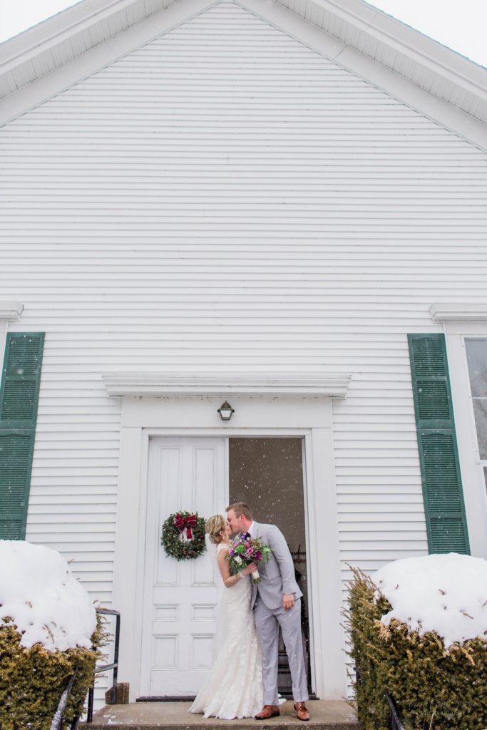 Bride and groom kissing on front steps of church in the snow