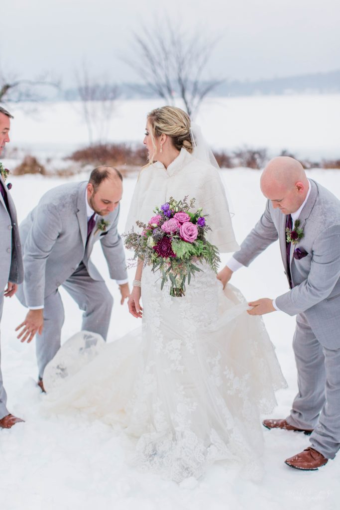 Groomsmen helping bride fluff her dress in the snow