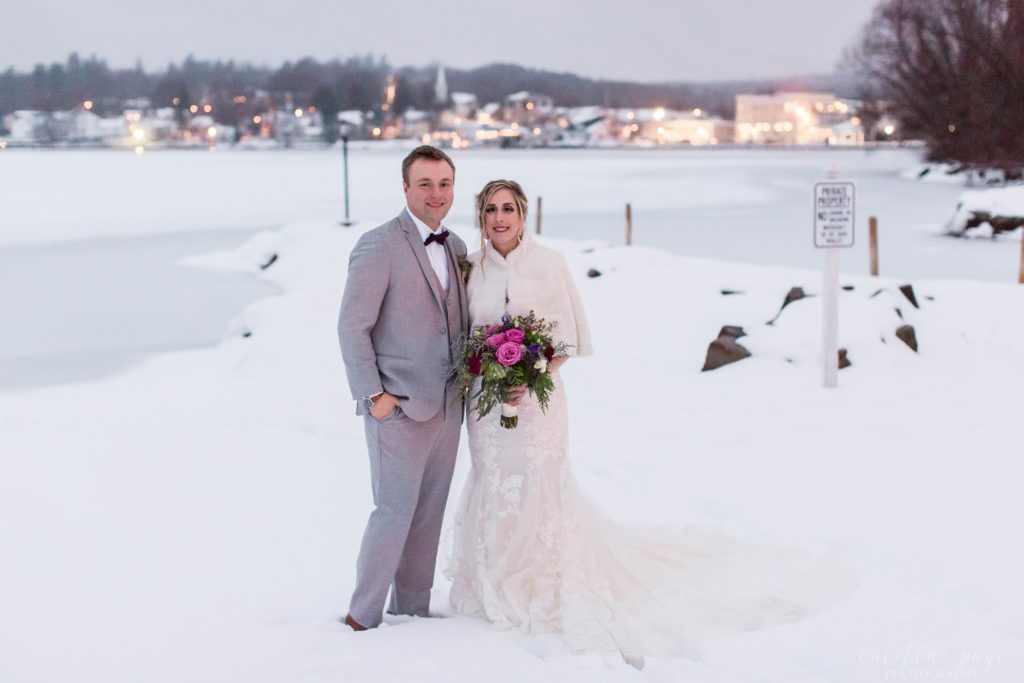 Portrait of bride and groom standing in the snow in front of lake