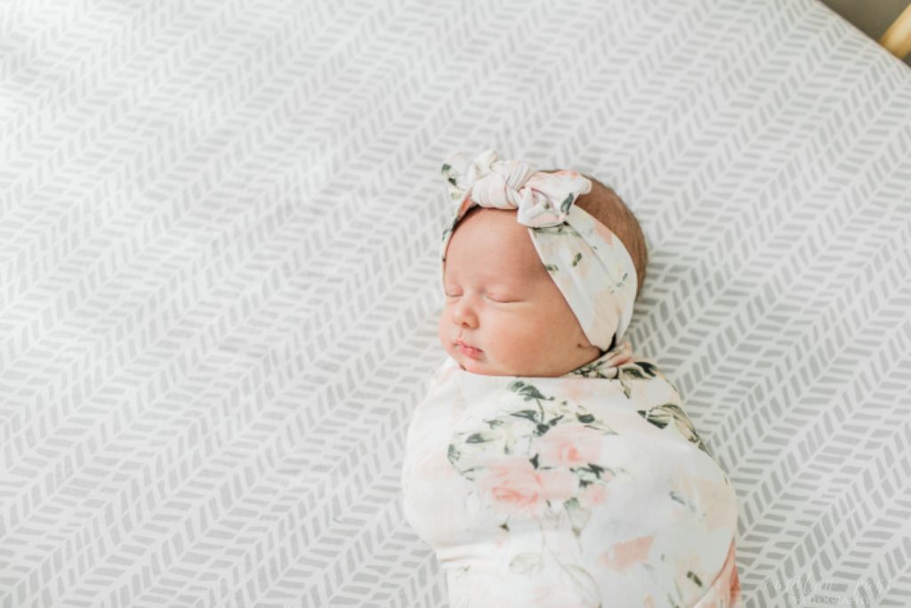 Newborn baby girl in floral swaddle in crib