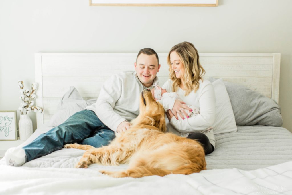 Parents and dog sitting on bed holding newborn baby girl