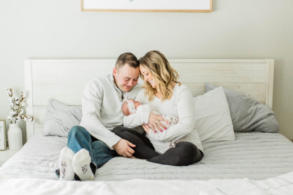 Parents sitting on bed holding newborn baby girl