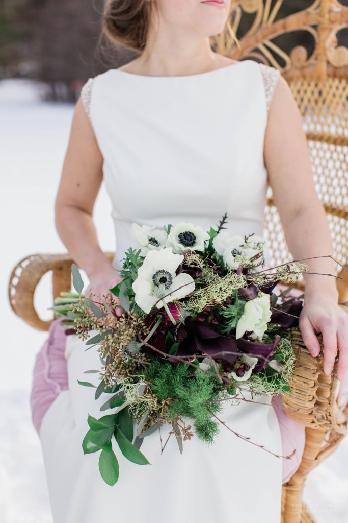 Winter bride holding bouquet of anemones and greens on her lap