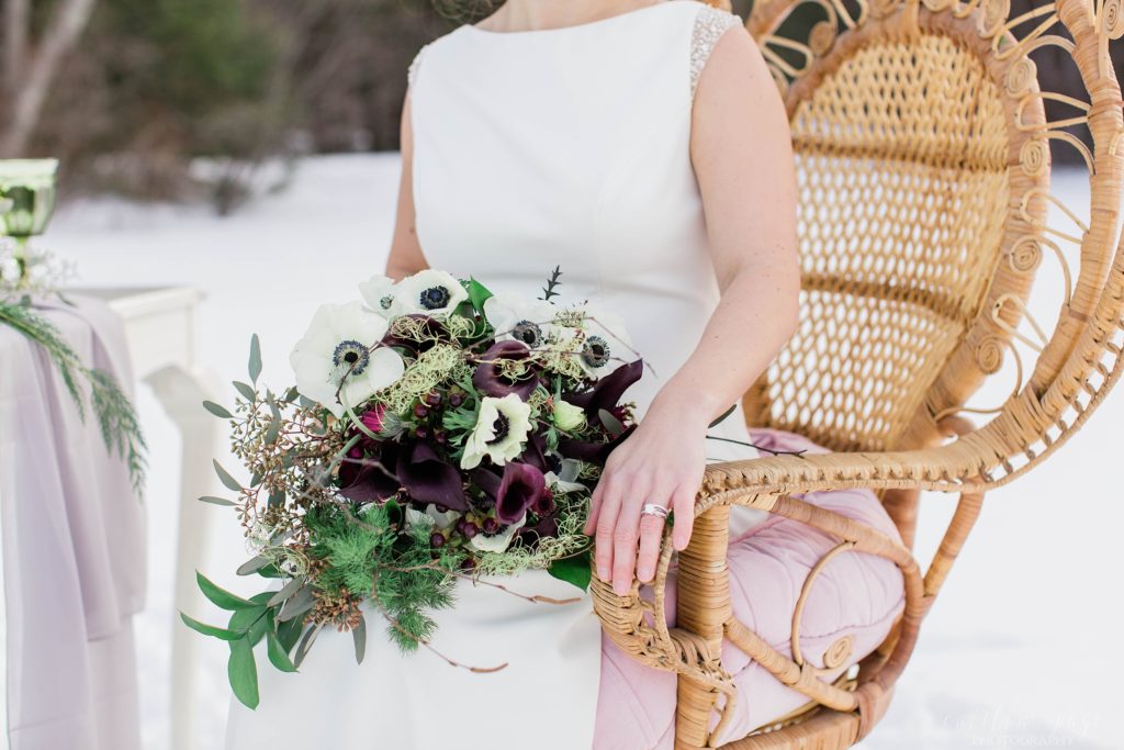 Winter bride holding bouquet of anemones and greens on her lap