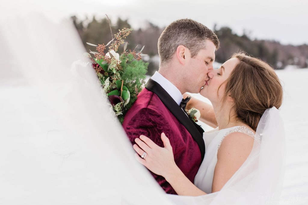 Bride and groom standing in the middle of a frozen lake with veil swooped in front of them