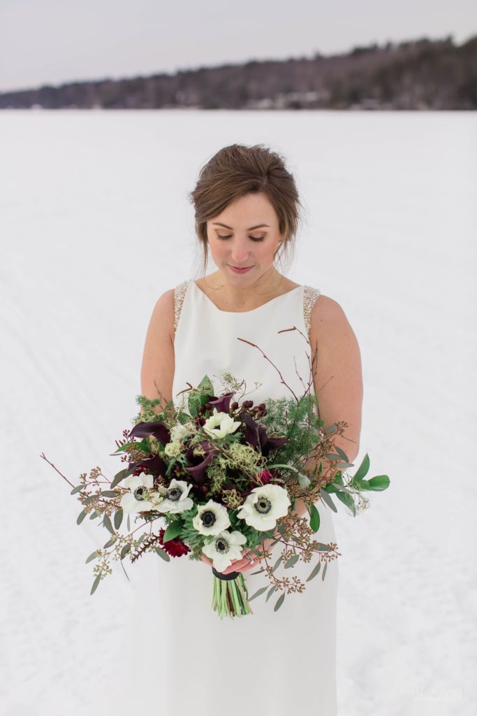 Winter bride holding textured bouquet of anenomes and greens in middle of frozen lake