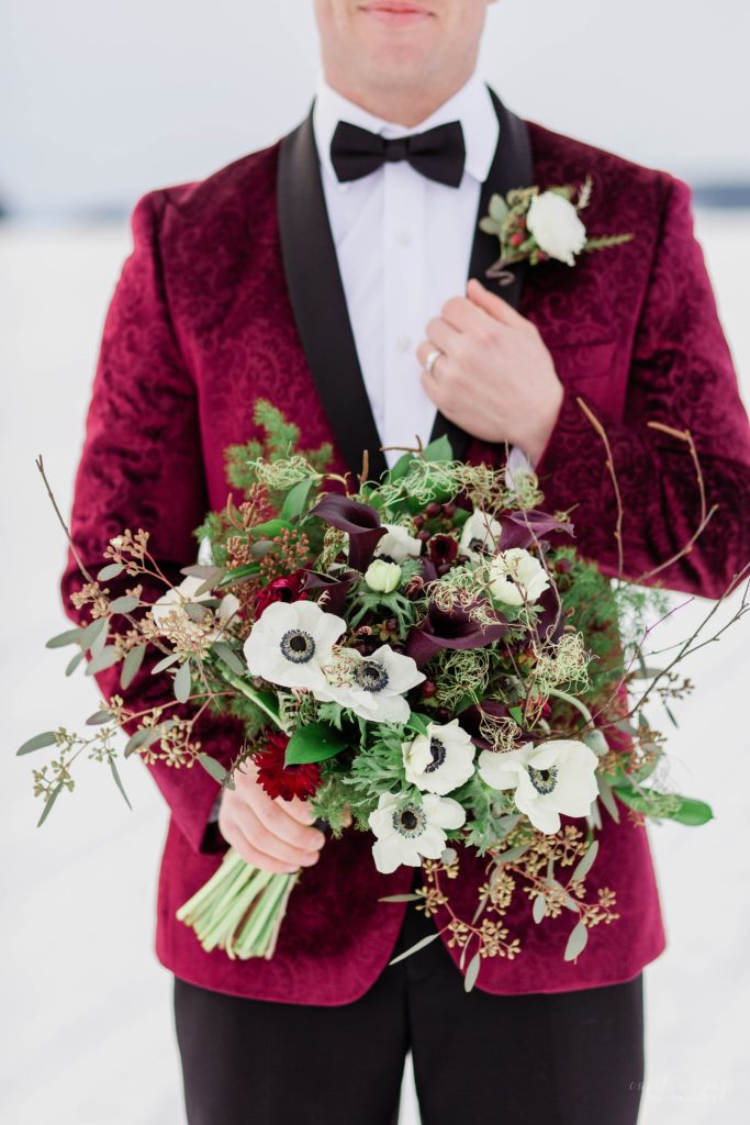 Groom in burgundy tuxedo jacket holding textured wedding bouquet