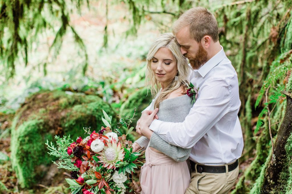 Man and woman snuggled together in the woods during romantic elopement