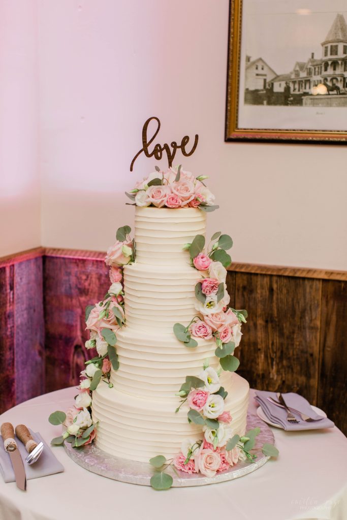 Four tiered white wedding cake with cascading pink and white flowers