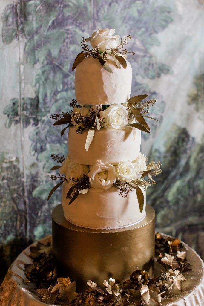 Three tiered wedding cake in front of hand painted backdrop