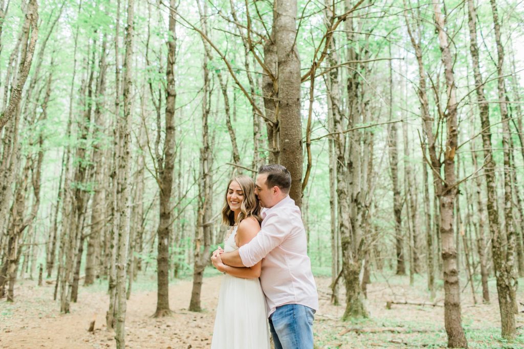 Man and woman snuggled together in the woods at engagement session