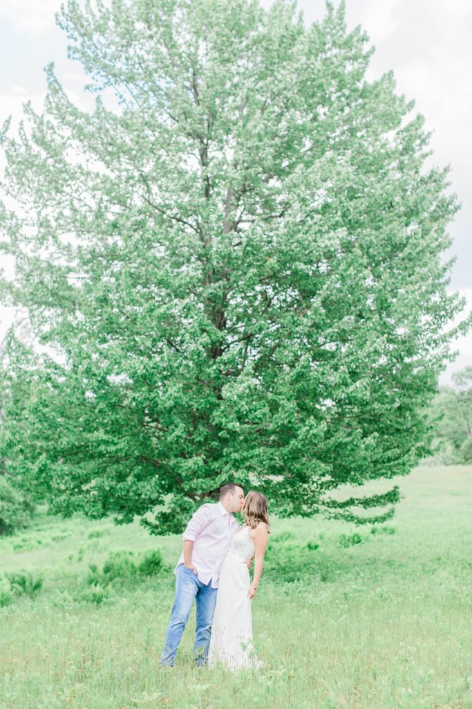 Man and woman kissing in front of large tree in a field