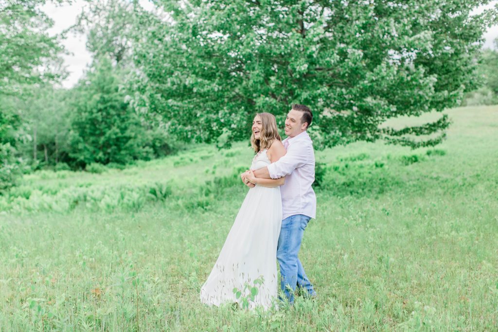 Man snuggling woman in front of a large tree in a field