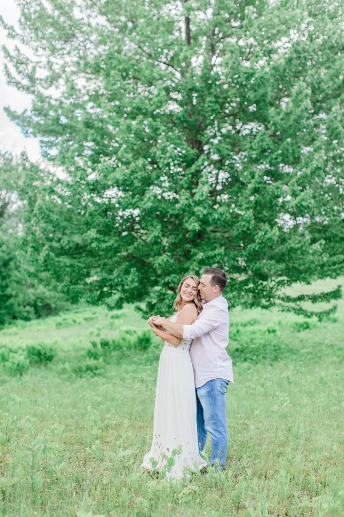 Man holding woman in front of a large tree in a field