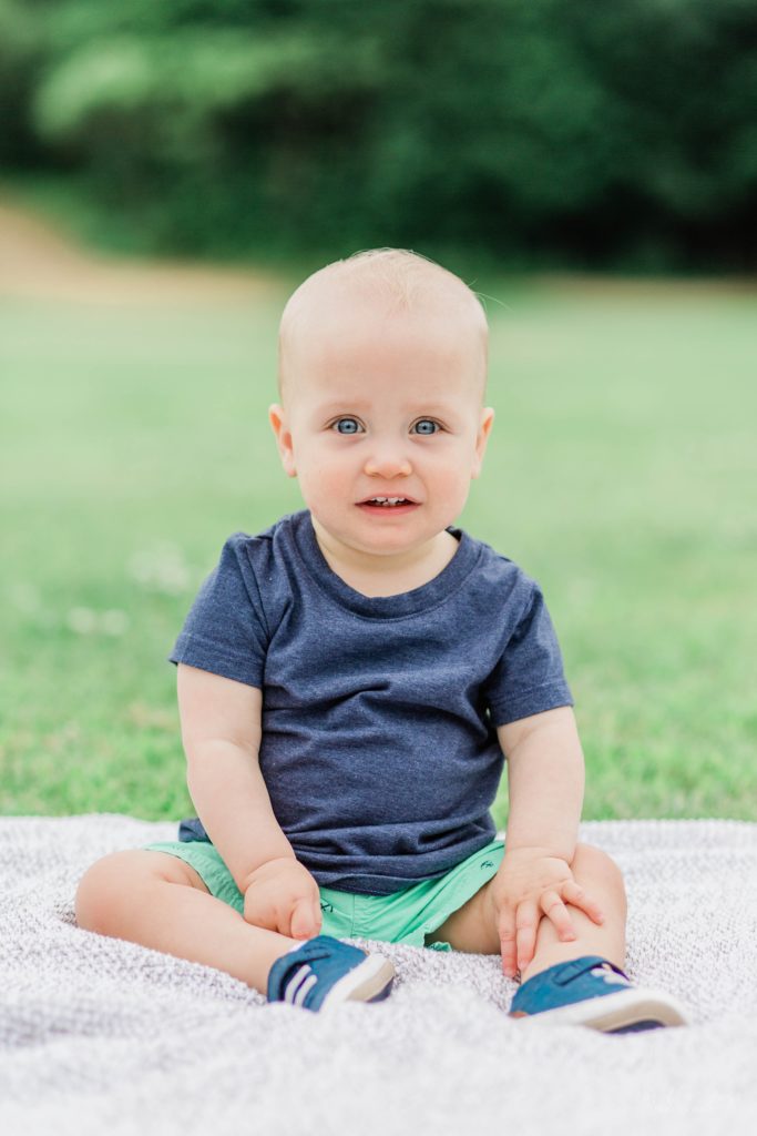 Toddler sitting on a gray blanket in the grass