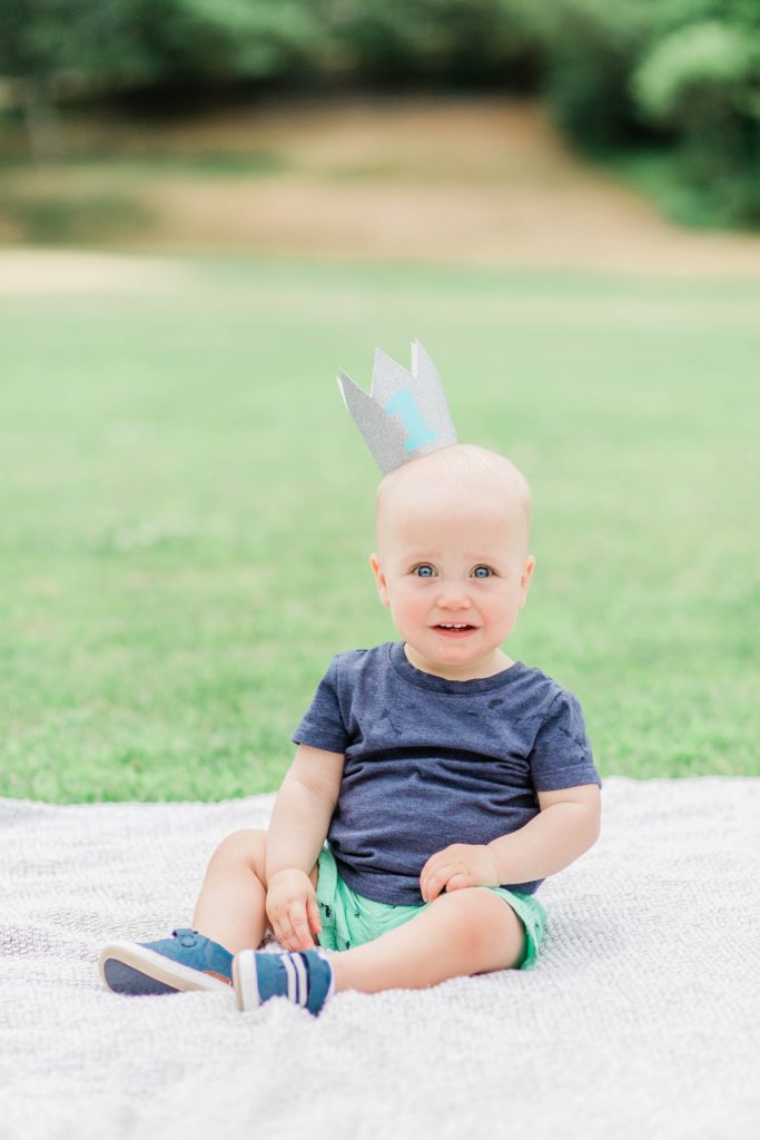 Toddler boy sitting on a blanket with a birthday crown
