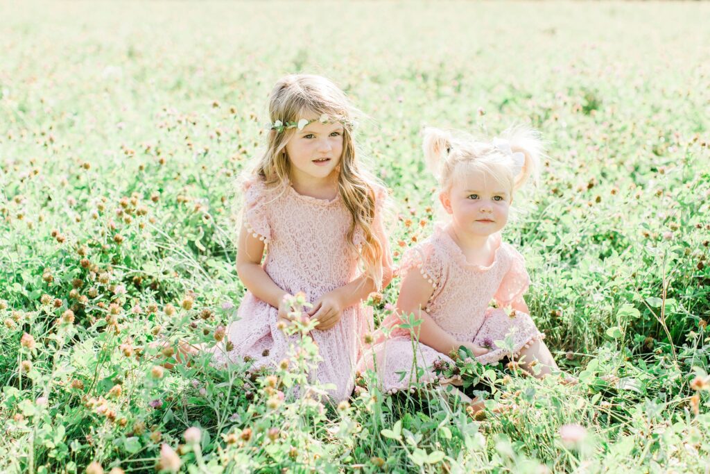 Little girls sitting in field in pink dresses