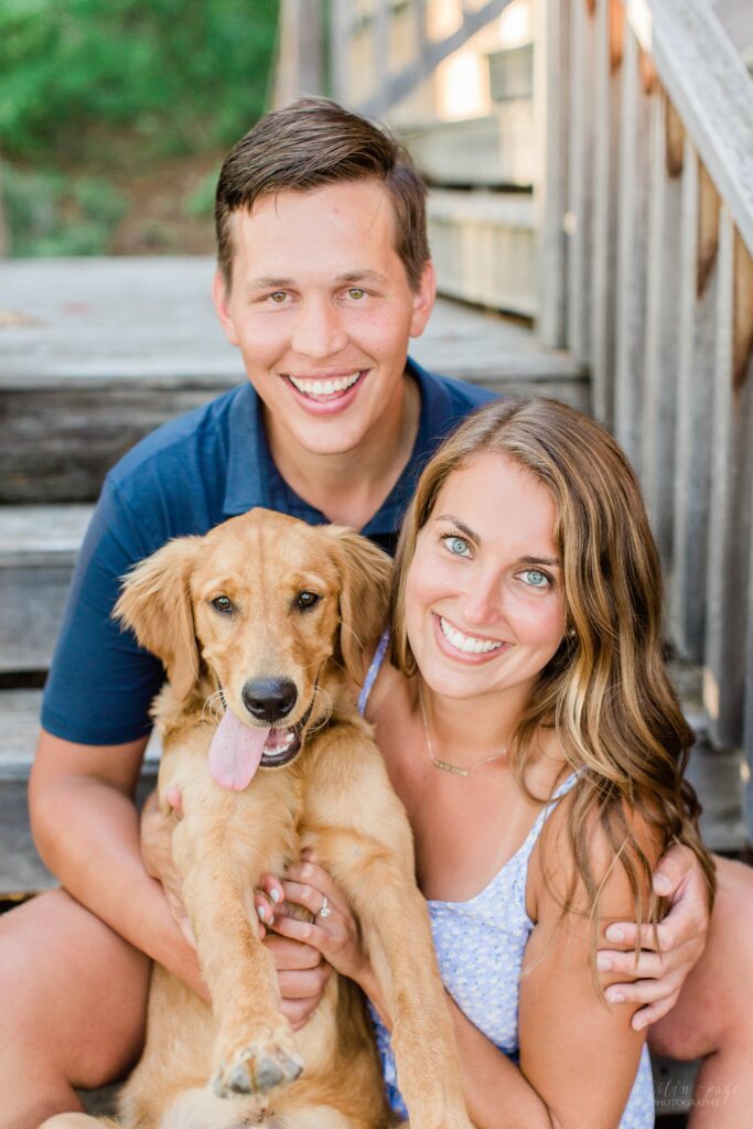 Man and woman sitting on wooden stairs holding golden retriever puppy