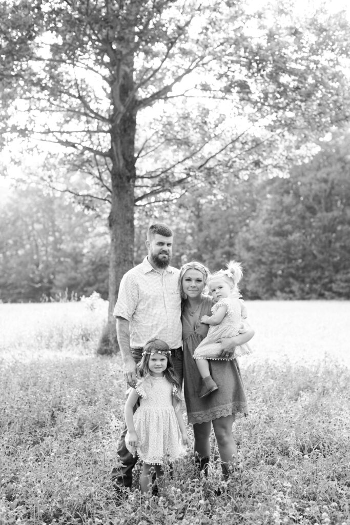 Black and white photo of young family standing under a tree in a field