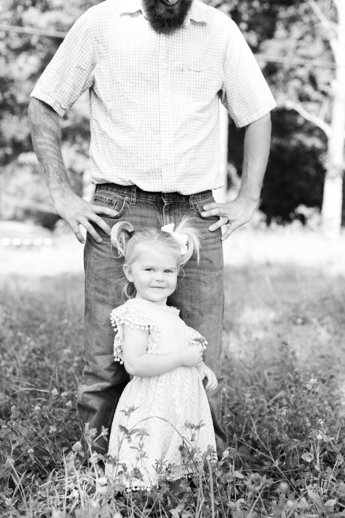 Black and white photo of little girl standing in front of her dad