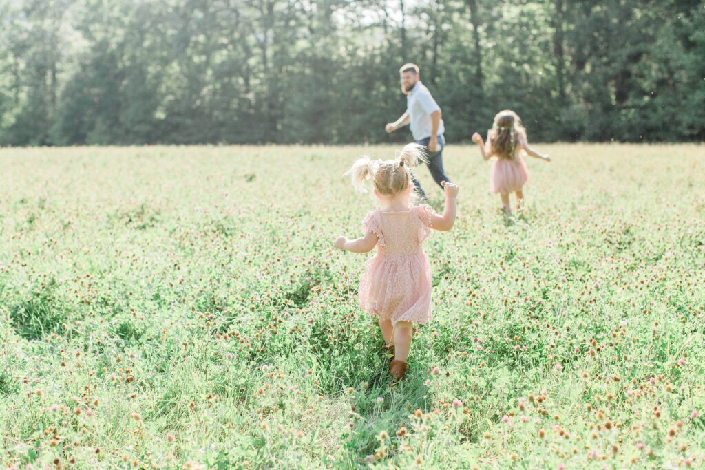 Little girls chasing their dad in a field