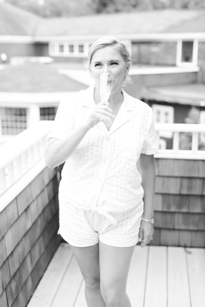 Black and white photo of bride drinking champagne in her pjs