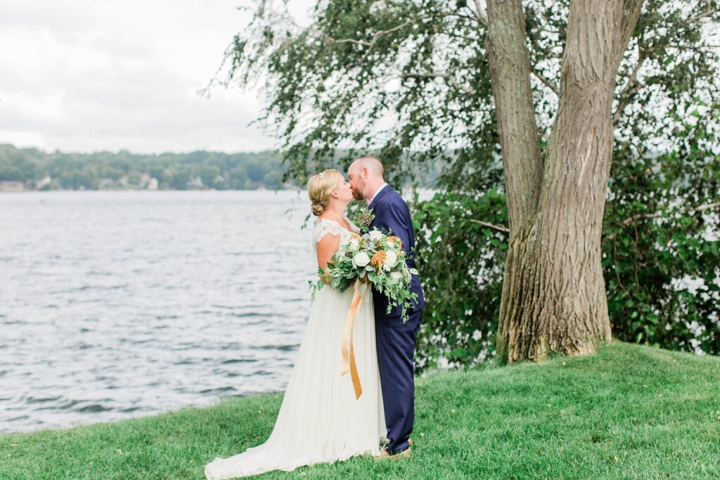 Portrait of bride and groom standing in front of Lake Winnipesaukee at Church Landing