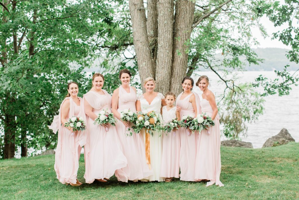 Bridesmaids standing together in front of Lake Winnipesaukee at Church Landing