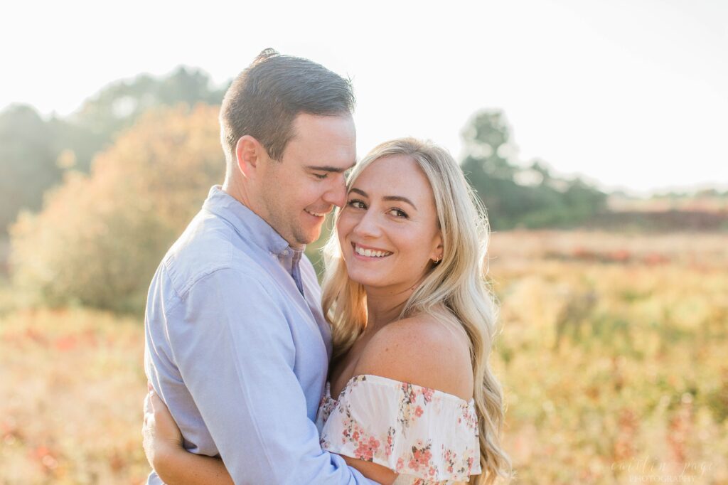 Couple snuggling together in field at sunset