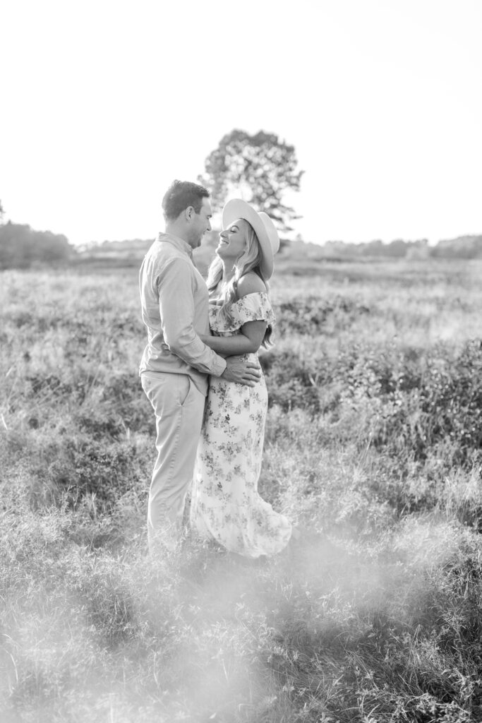 Black and white photo of man and woman standing together in field at sunset