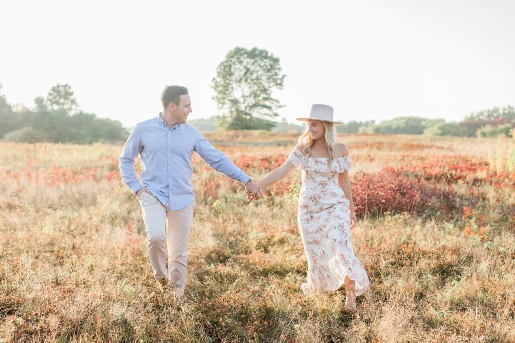 Man and woman walking through field at sunset holding hands