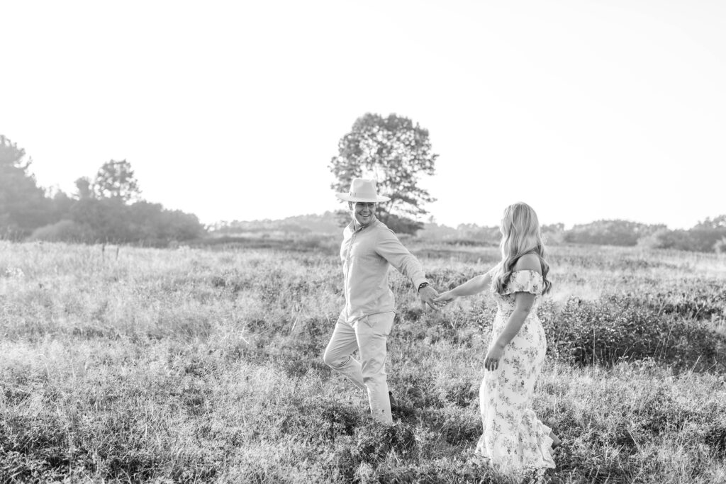 Black and white photo of man leading woman through field at sunset