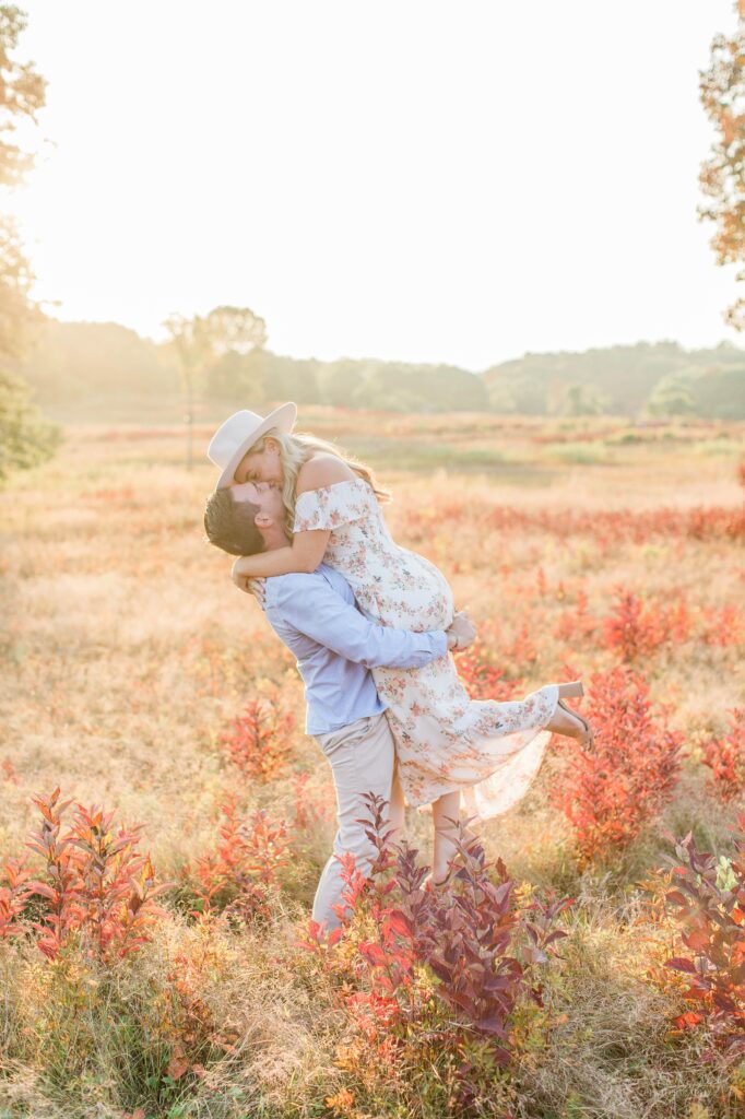 Man holding woman in the air in a field at sunset