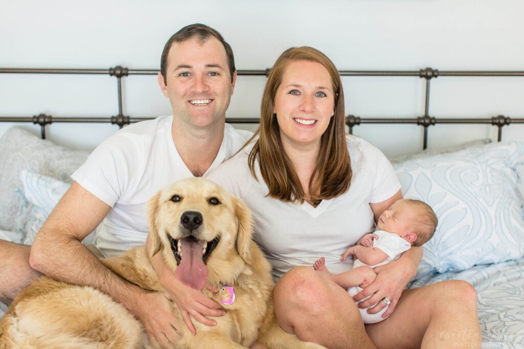 Parents with newborn and dog sitting on bed