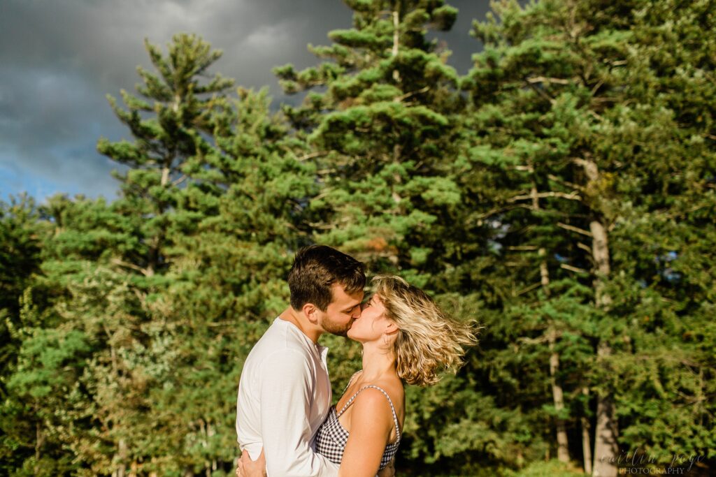 Man and woman kissing in front of dark sky and woods